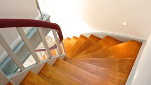 A wooden staircase with a skylight above, leading to a room with white walls and a red railing.