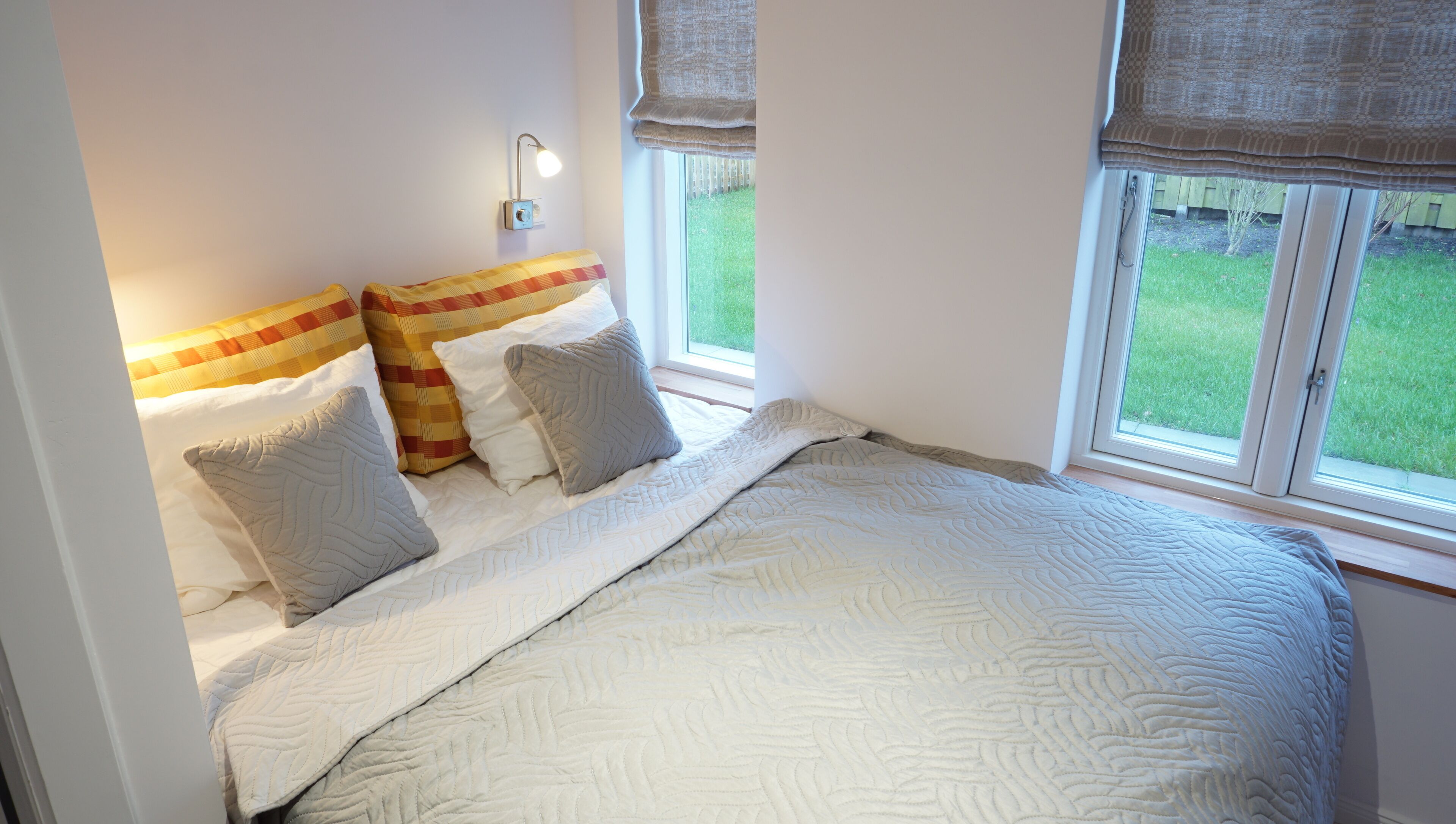 A bedroom with a bed, pillows, a nightstand, a lamp, and a window with a view of a grassy yard.