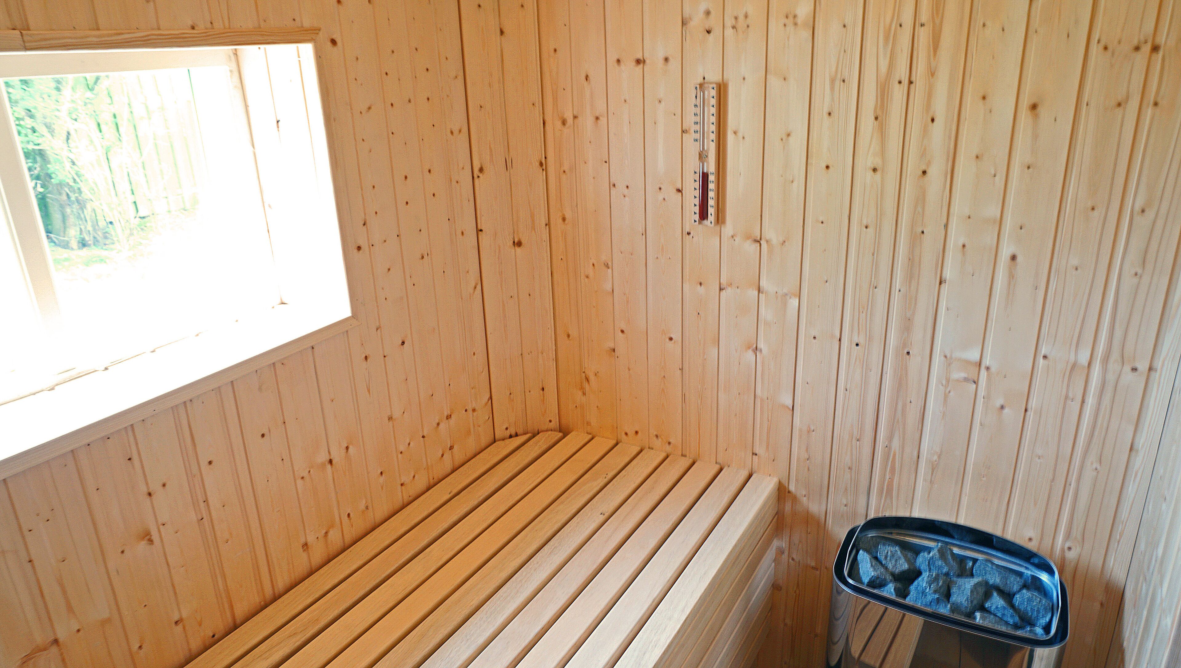 A sauna room with wooden walls, a bench, and a thermometer on the wall.