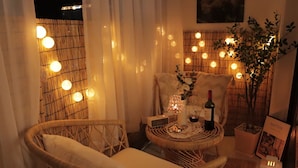 A cozy room with wicker chairs, a small round table with a bottle of wine, a lamp, and a potted plant. - Morning Madrid (Jeju City)