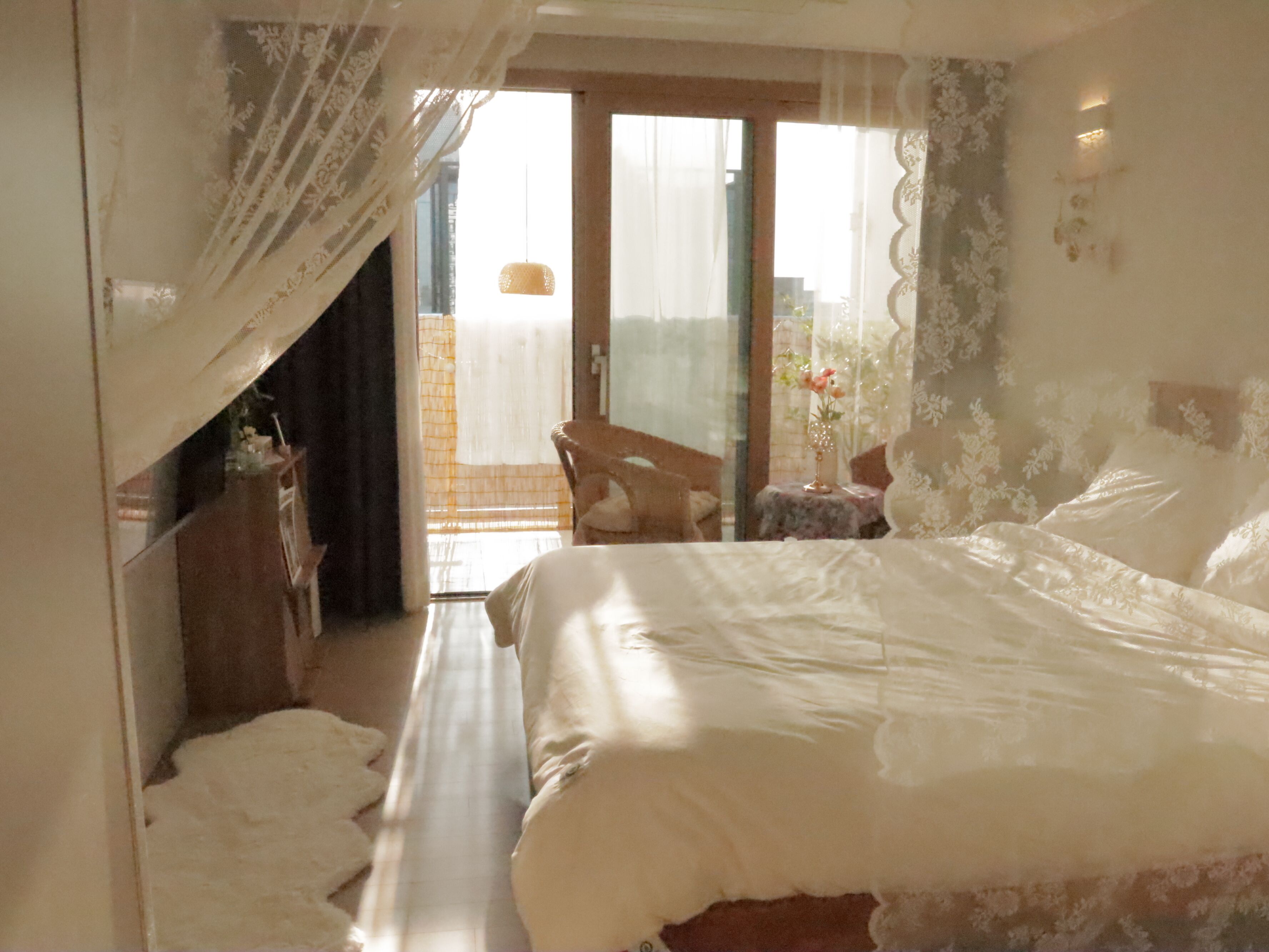 A bedroom with a large bed, a chair, a small table with a vase, and a balcony with a view.