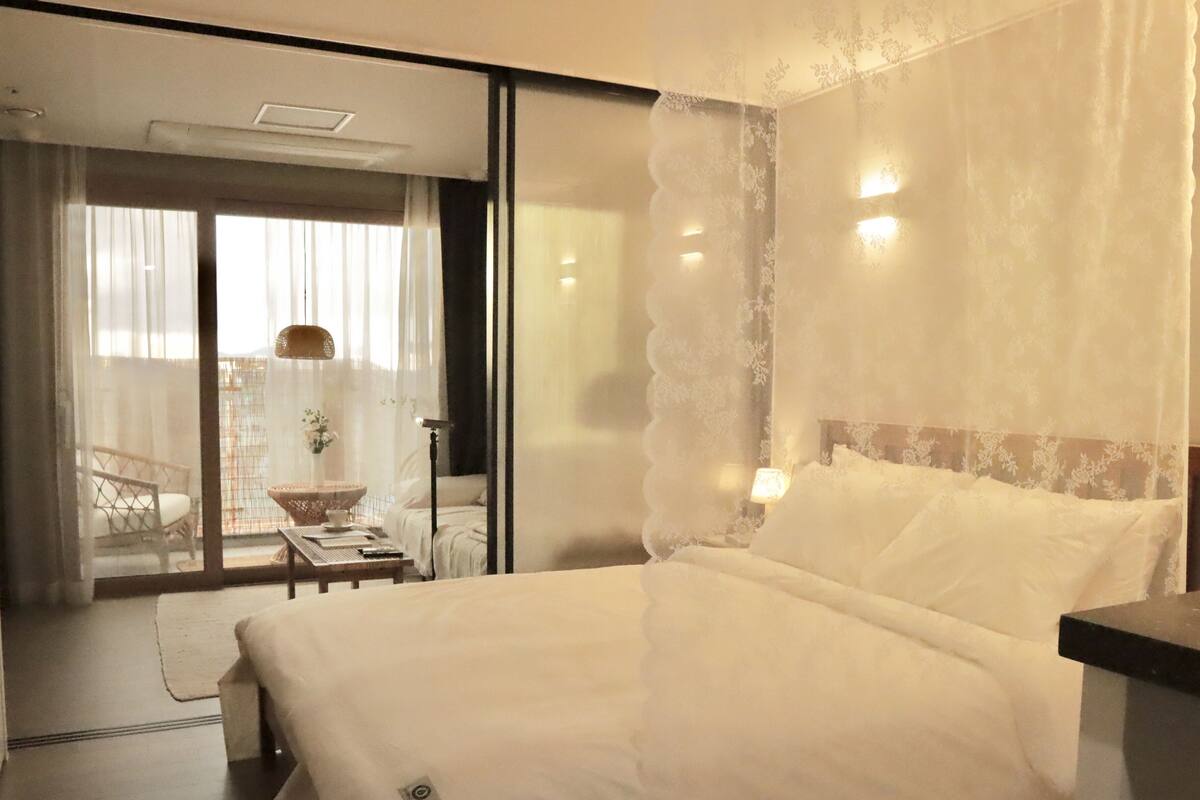 A hotel room with a large bed, a bedside table, a lamp, and a view of the balcony.
