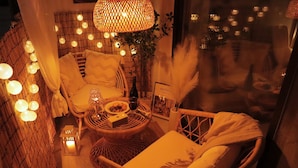 A cozy indoor seating area with wicker furniture, a table with a bottle and glasses, and string lights. - Morning Madrid (Jeju City)