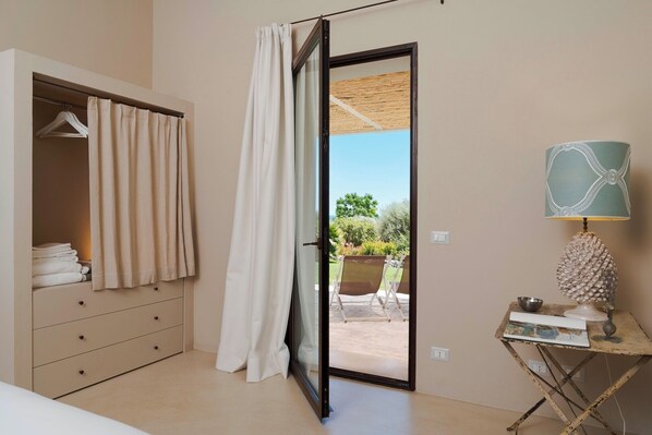 Un dormitorio con armario, puerta corredera de vidrio que da a un espacio exterior y una mesita con lámpara.