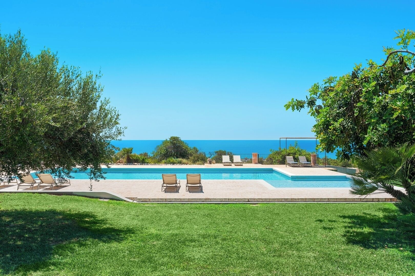 Une piscine entourée de chaises longues, de verdure et offrant une vue dégagée sur l’océan.