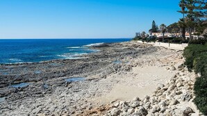 En klippefyldt strand med krystalklart hav og en række huse langs kysten.