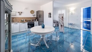 Een moderne keuken met witte kasten, een roestvrijstalen koelkast en een eethoek met een witte tafel en transparante stoelen.