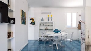 Een eetgedeelte met een ronde tafel, transparante stoelen en een blauwe betegelde vloer.