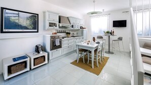 Una cocina moderna con muebles blancos, un comedor con mesa y sillas, horno empotrado y televisor de pantalla plana montado en la pared.