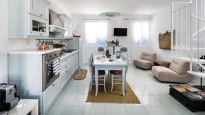 Una cocina moderna con armarios blancos, un área de comedor con mesa y sillas, un sofá y una escalera.
