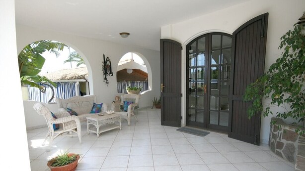 A spacious patio with white wicker furniture, a stone wall, and a large arched door. - Villa Trapezio with private pool and tennis court (Quartu Santa Elena)