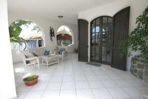 A spacious patio with white wicker furniture, a stone wall, and a large arched door. - Villa Trapezio with private pool and tennis court (Quartu Santa Elena)