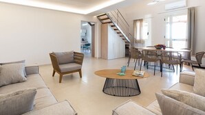 Een moderne woonkamer met een bank, fauteuils, een salontafel en een eethoek met rieten stoelen.