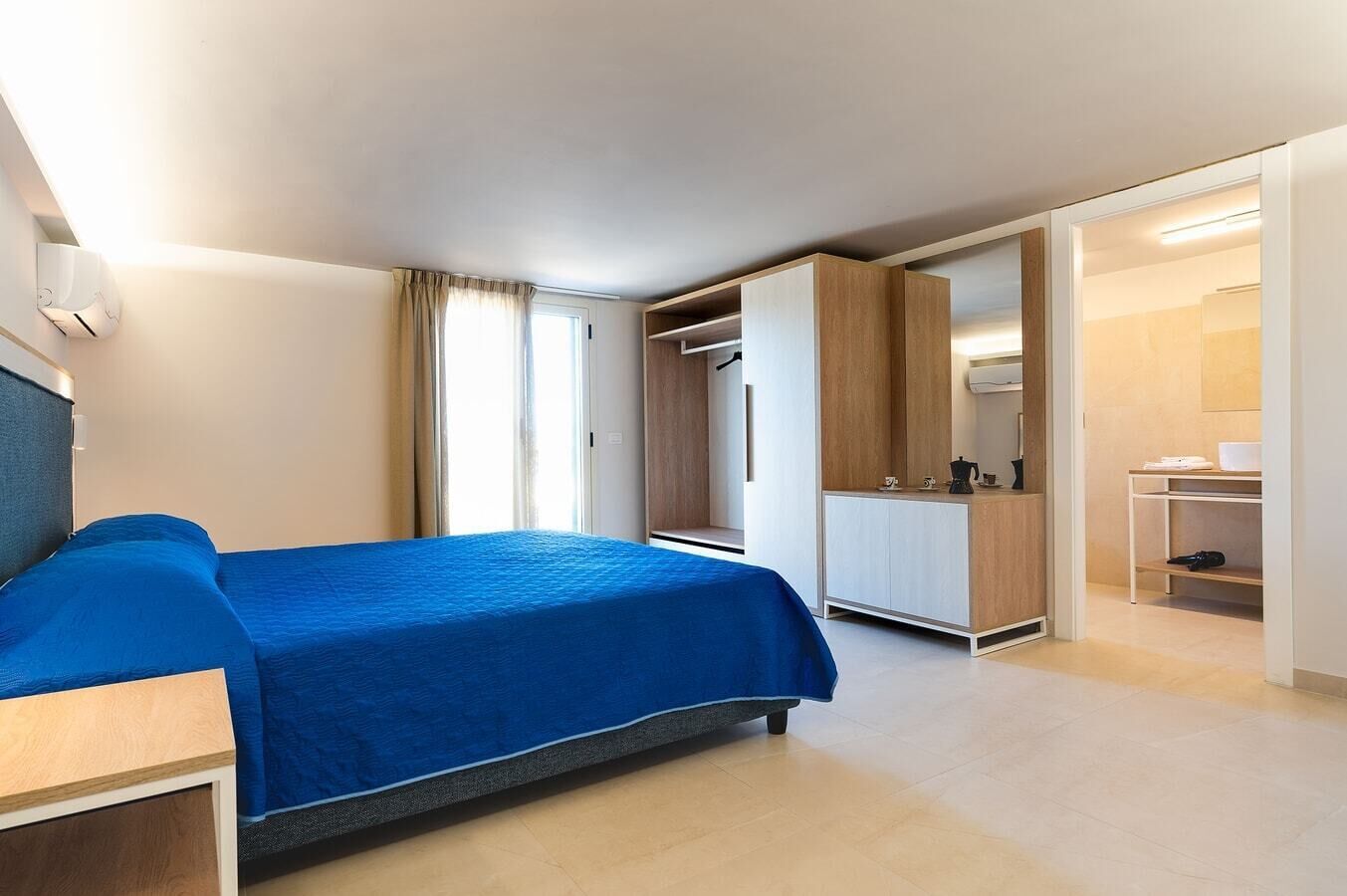 A modern hotel room with a bed, a desk, a wardrobe, and a bathroom.
