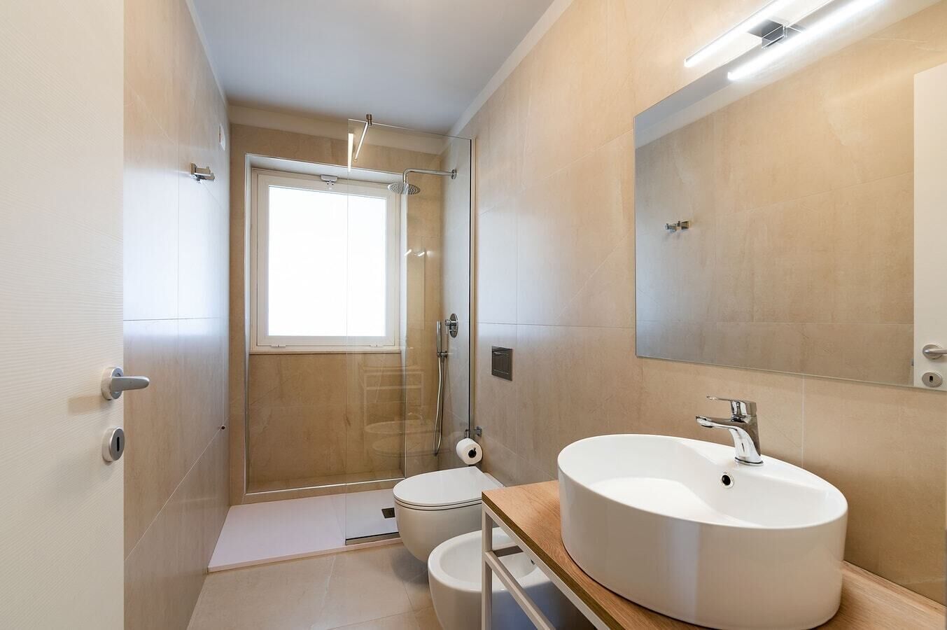 Une salle de bain moderne avec une douche à parois de verre, un lavabo rond et un grand miroir.