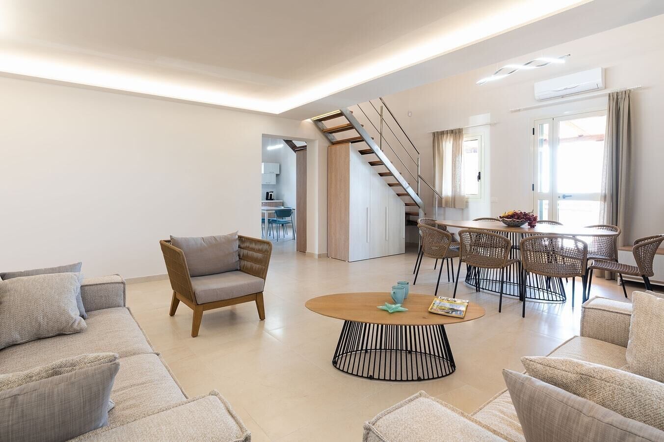 En moderne stue med sofa, lænestole, et sofabord og et spiseområde med fletstole.
