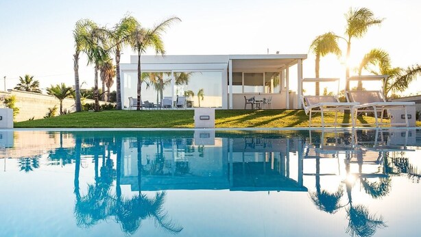 Un hotel moderno con piscina, palmeras y cielo despejado.