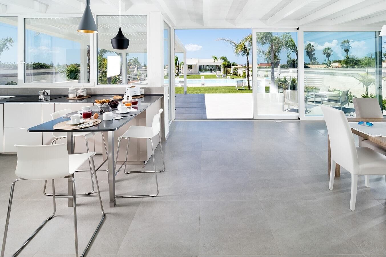 A modern kitchen with a dining area, large windows, and a view of a pool and greenery.