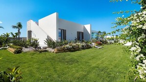 Un edificio moderno y blanco con una escalera que conduce a la entrada, rodeado de follaje y plantas florecientes bien cuidadas.