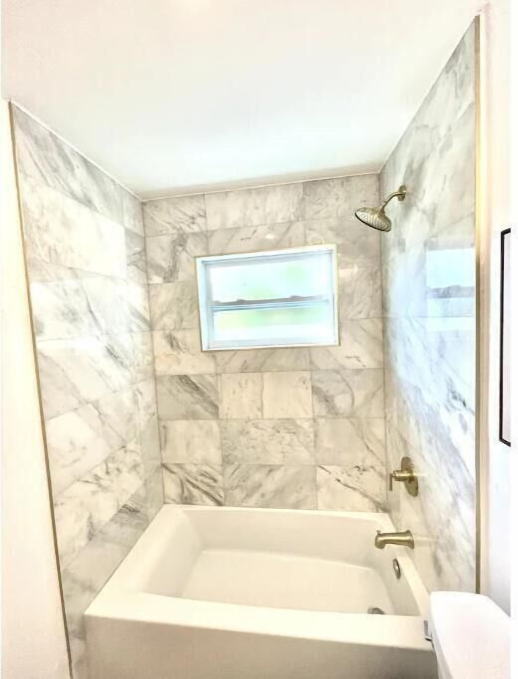 A bathroom with a marble wall, a bathtub, and a framed picture.