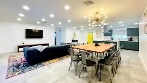 A modern living room with a sofa, dining table, and chairs. There is a kitchen area with cabinets and a sink.