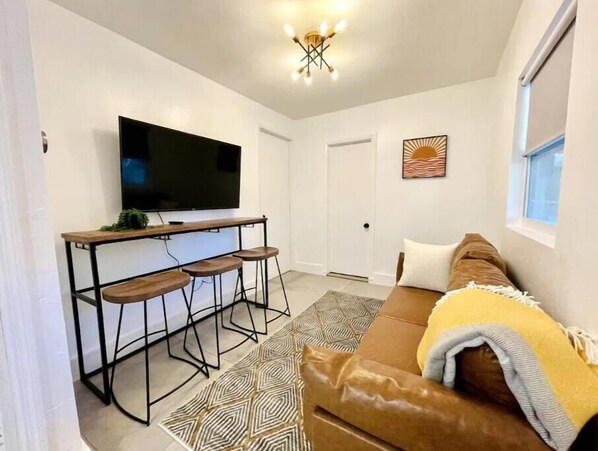 Una sala de estar con un sofá de cuero marrón, un televisor montado en un mueble de madera y un tapete estampado.