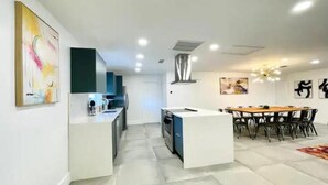 A modern kitchen with a central island, a dining area with a wooden table and chairs, and artwork on the walls.