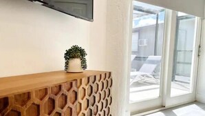 A room with a wooden console table, a potted plant, and a large window with a view of outdoor seating.