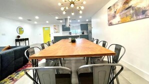 A modern dining area with a wooden table and metal chairs, a sofa, and a kitchen in the background.
