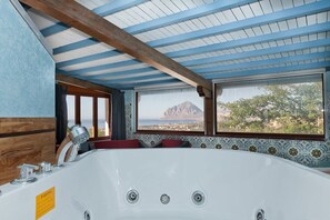 Ein Badezimmer mit einer großen Badewanne, Holzbalkendecke und Blick auf Berg und Meer.