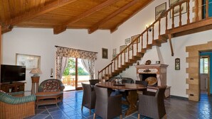 A spacious living room with a wooden ceiling, a dining area with wicker furniture, a television, and a staircase leading to an upper level. - Villa San Vito - Private villa with pool (Valderice)