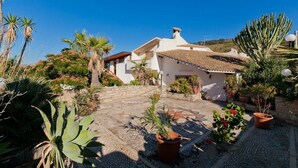 A white villa with a tiled roof, surrounded by a garden with various plants and a stone pathway leading to the entrance. - Villa San Vito - Private villa with pool (Valderice)