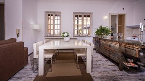 Un espace repas moderne avec une table blanche, deux fenêtres, un canapé marron et un buffet en bois rustique.