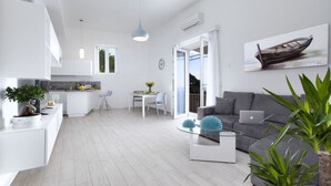 Ein modernes Wohnzimmer mit grauem Sofa, einem Glastisch und einem Essbereich mit weißem Tisch und Stühlen.