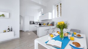 Eine moderne Küche mit weißen Schränken, einer zentralen Kochinsel und einem Essbereich mit einem für das Frühstück gedeckten Tisch.