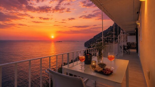 Ein Balkon mit Sonnenuntergangsblick, ein Tisch mit Gläsern und Oliven sowie ein Stuhl.