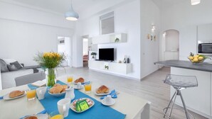 Eine moderne Küche mit Fernseher, weißen Schränken und einer Essecke mit Frühstücksangebot.