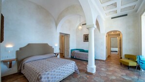 Un ampli dormitori amb un llit gran, un sofà i una cadira. Hi ha diverses portes que condueixen a altres habitacions.