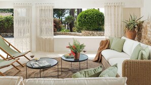 A cozy outdoor seating area with a wicker sofa, a round table, and a chair, surrounded by white curtains and a view of greenery. - Villa Rossana, with pool near the sea (Plemmirio)