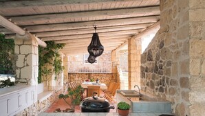 A rustic outdoor kitchen with stone walls, wooden furniture, and a hanging light fixture. - Villa Rossana, with pool near the sea (Plemmirio)