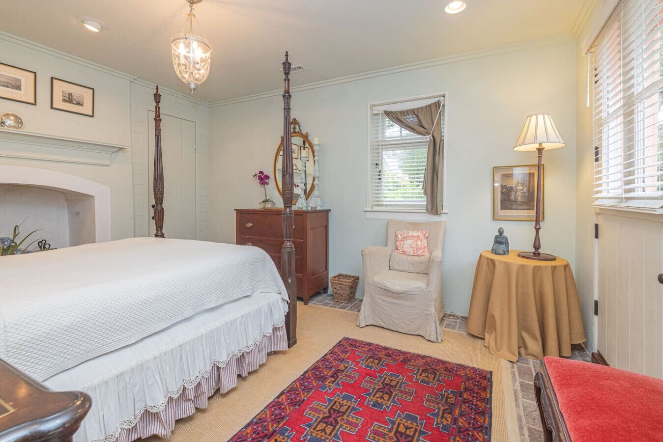 A bedroom with a bed, dresser, chair, table, and a fireplace.