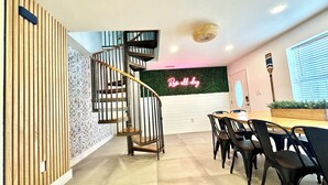Un interior moderno con una escalera espiral, un letrero de neón, una zona de comedor con sillas y una pared verde.