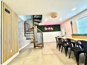 Ein modernes Interieur mit einer Wendeltreppe, einer Neonreklame, einem Essbereich mit Stühlen und einer grünen Wand.