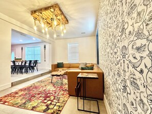 En moderne stue med sofa, tapetvæg, lysekrone samt spiseområde med stole og bord.