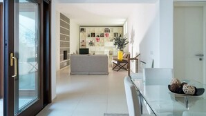 A modern living room with a glass door leading to a balcony, a sofa, a coffee table, and a bookshelf filled with various items.