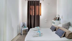 A hotel room with a bed, a chair, a nightstand, and a window with curtains.