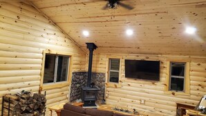 A log cabin interior with a fireplace, wooden walls, a ceiling fan, and a sofa. - Cabin getaway on the Menominee River  (Wallace)