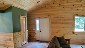 A wooden cabin interior with a green wall, a wooden door, a window, and a couch. - Cabin getaway on the Menominee River  (Wallace)