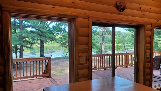 A wooden cabin with large windows overlooking a lake, a deck, and a table. - Cabin getaway on the Menominee River  (Wallace)