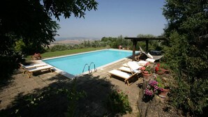 Una piscina amb gandules i una pèrgola, envoltada de vegetació i amb vista a les colines.